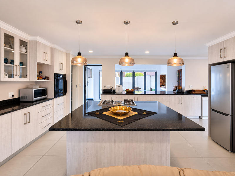 Modern kitchen featuring a large central island with granite countertops, built-in oven, gas hob, and ample cabinetry, illuminated by stylish pendant lighting.