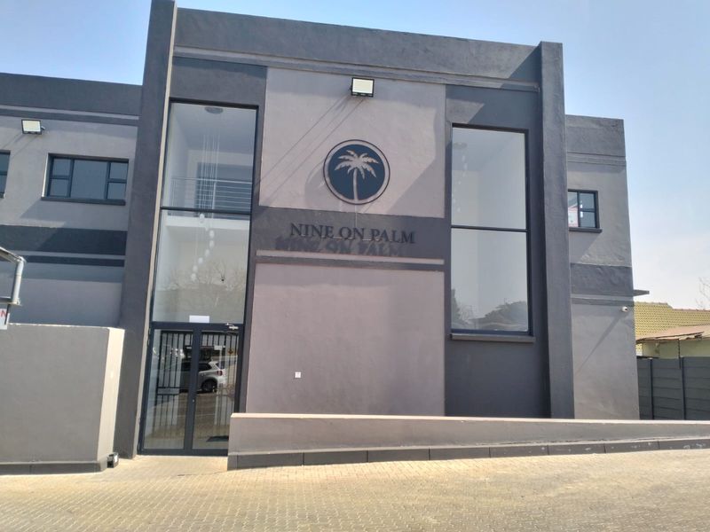 Modern office building facade featuring a contemporary grey finish, double-height glass windows, and prominent signage at the entrance.