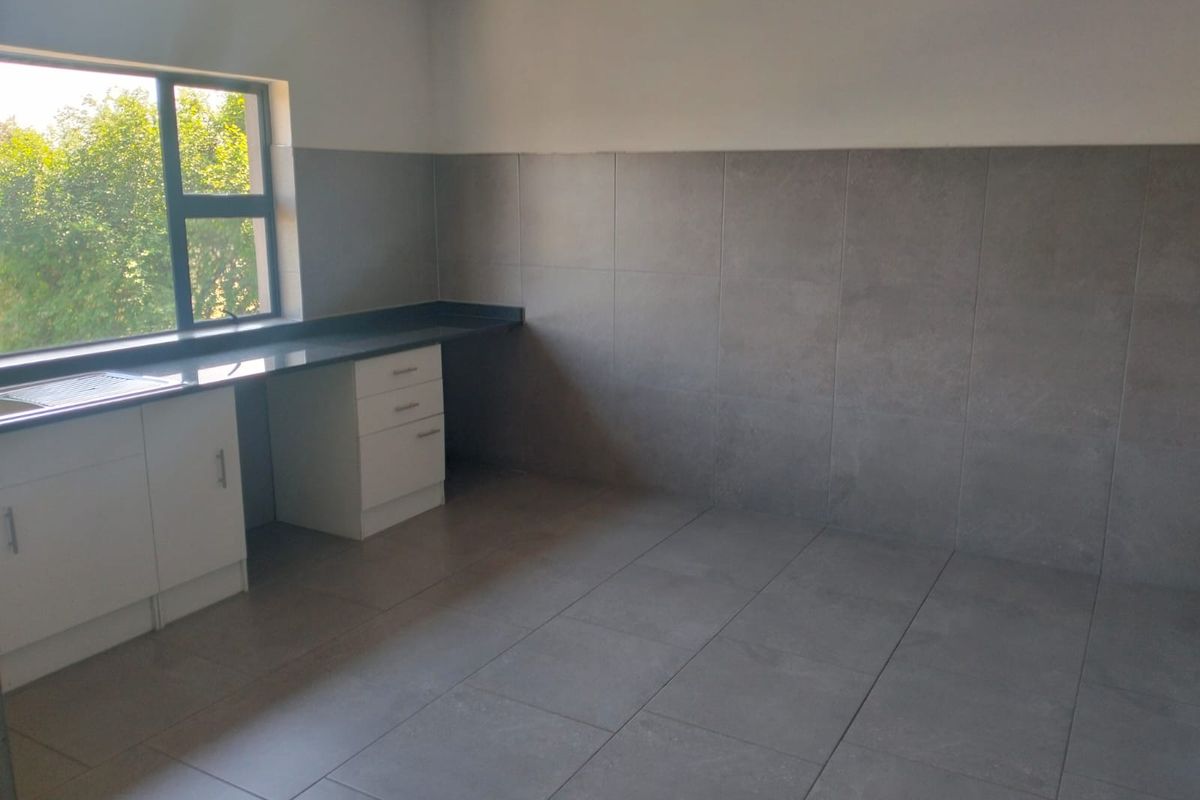 A clean, empty kitchen space featuring modern grey floor and wall tiles, white built-in cabinetry, and a dark granite countertop with a sink.