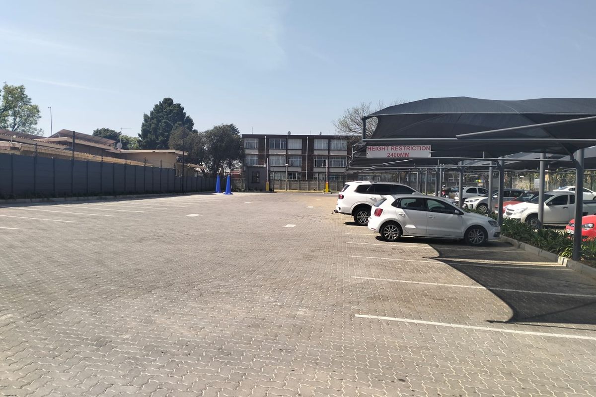 A well-maintained paved parking area featuring a covered carport structure with height restrictions and secure perimeter fencing.