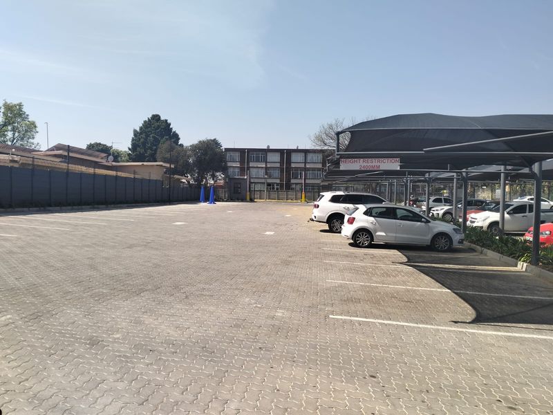 A well-maintained paved parking area featuring a covered carport structure with height restrictions and secure perimeter fencing.