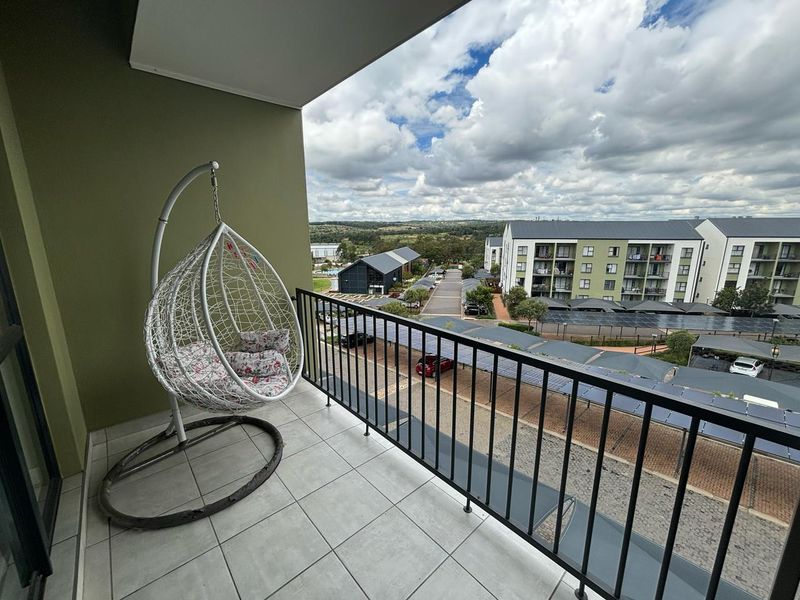 A covered balcony featuring tiled flooring and a metal balustrade, offering an elevated view of the surrounding residential complex and landscape.
