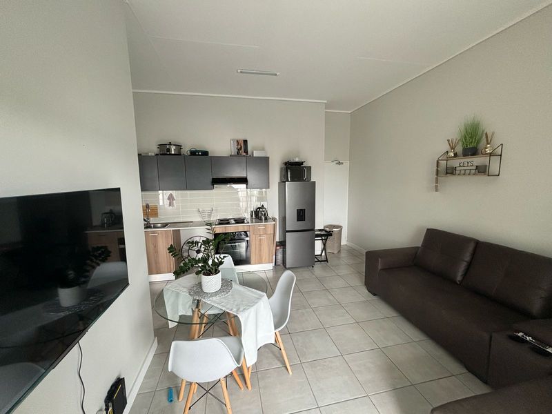 Open-plan living area featuring a compact kitchen with modern cabinetry, integrated appliances, and neutral tiled flooring throughout the combined space.