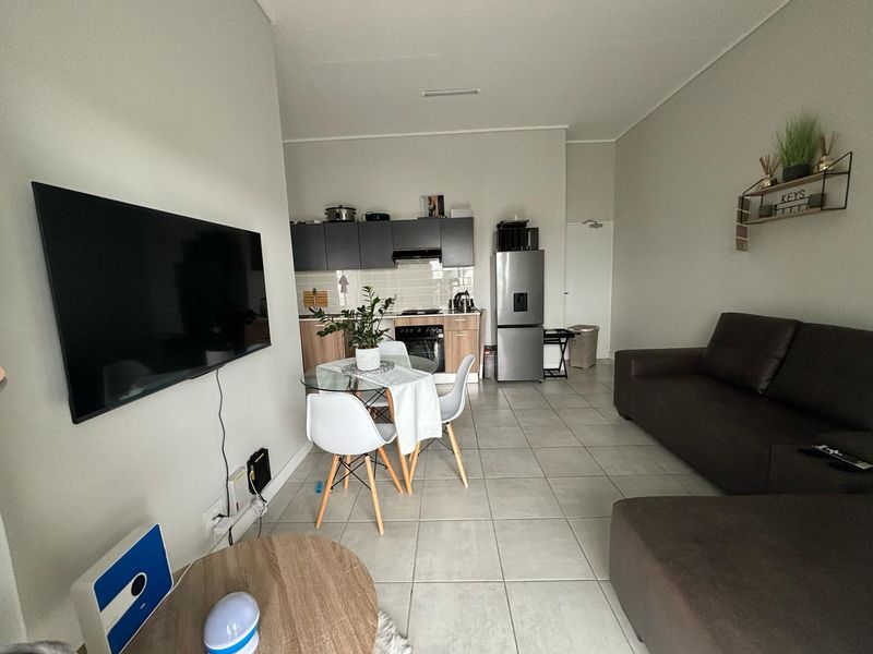 Open-plan living area featuring a modern kitchen with built-in cabinetry, oven, and hob, seamlessly flowing into the dining and lounge space with tiled flooring.