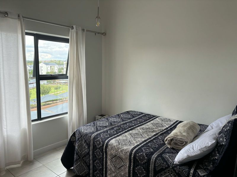 A bright bedroom featuring tiled flooring, a large aluminium-framed window with natural light, and a simple pendant light fixture.
