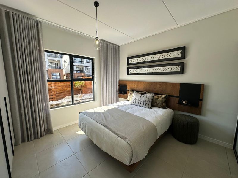 A well-maintained bedroom featuring tiled flooring, a modern built-in headboard, and large aluminium-framed windows allowing for natural light.