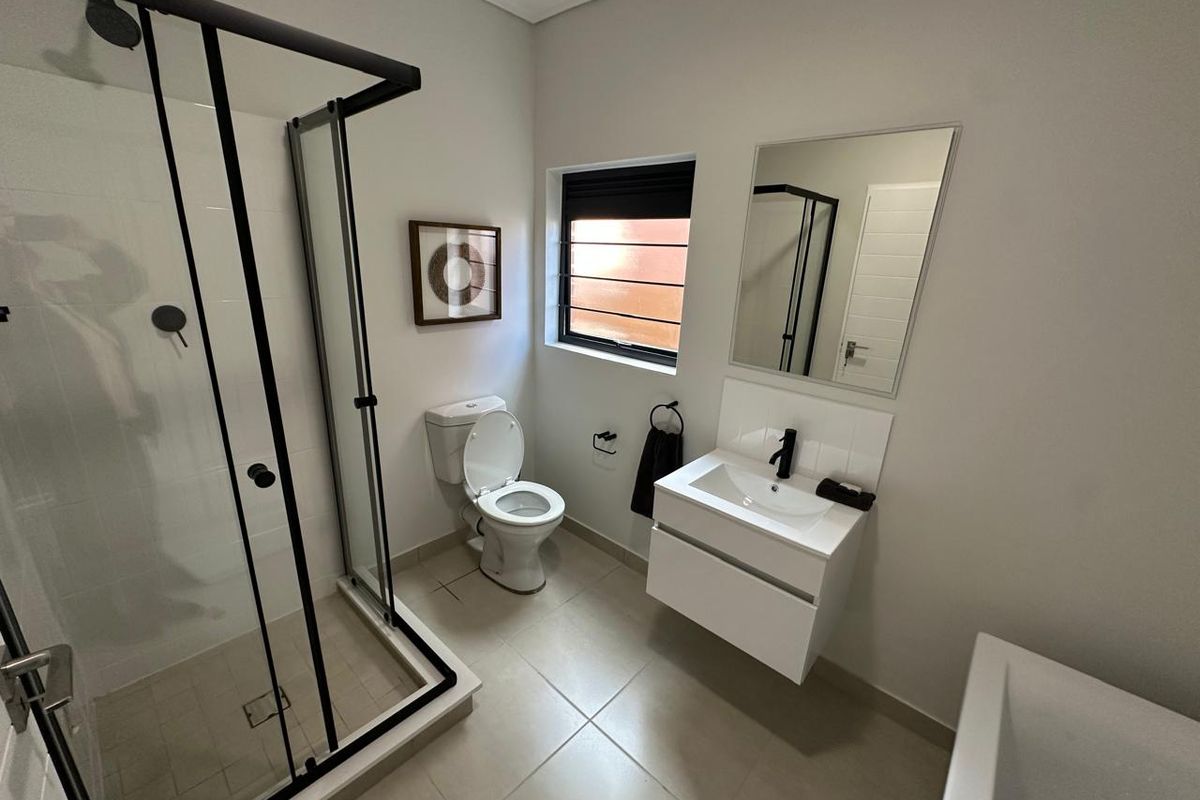 Modern bathroom featuring a glass-enclosed shower, wall-mounted vanity with basin, toilet, and neutral floor tiling.