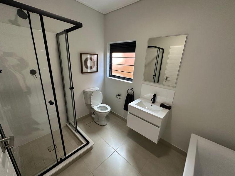 Modern bathroom featuring a glass-enclosed shower, wall-mounted vanity with basin, toilet, and neutral floor tiling.
