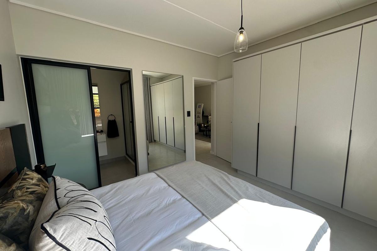 Modern bedroom featuring extensive built-in cupboards, sleek sliding door access to an en-suite bathroom, and contemporary pendant lighting.