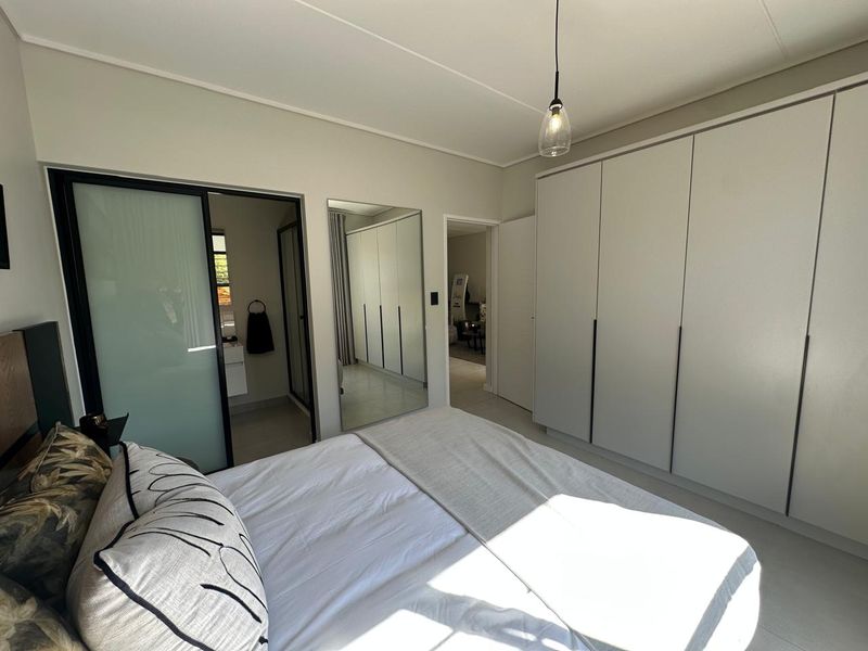 Modern bedroom featuring extensive built-in cupboards, sleek sliding door access to an en-suite bathroom, and contemporary pendant lighting.