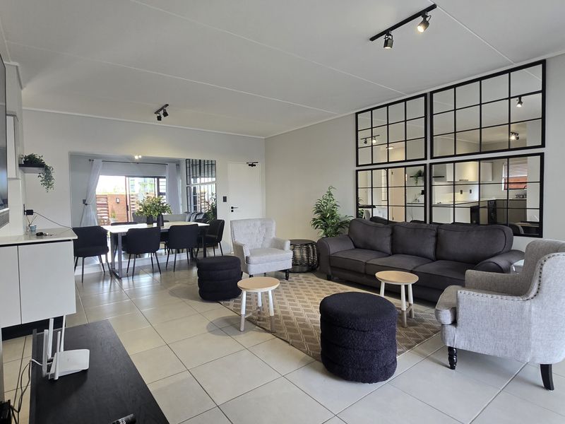 Spacious open-plan living and dining area featuring neutral tiled flooring, modern track lighting, and large decorative wall mirrors, creating a bright and airy atmosphere.