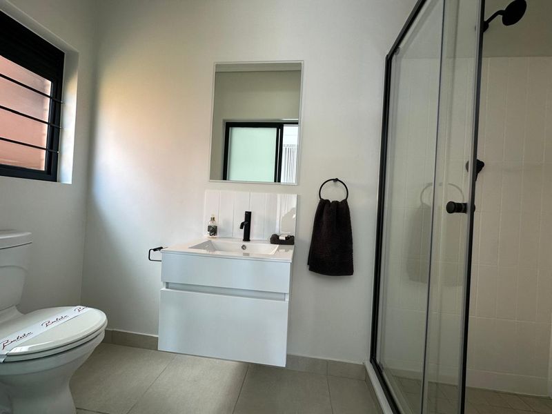 Modern bathroom featuring a wall-mounted vanity with a black faucet, a glass-enclosed shower, and neutral floor tiling.