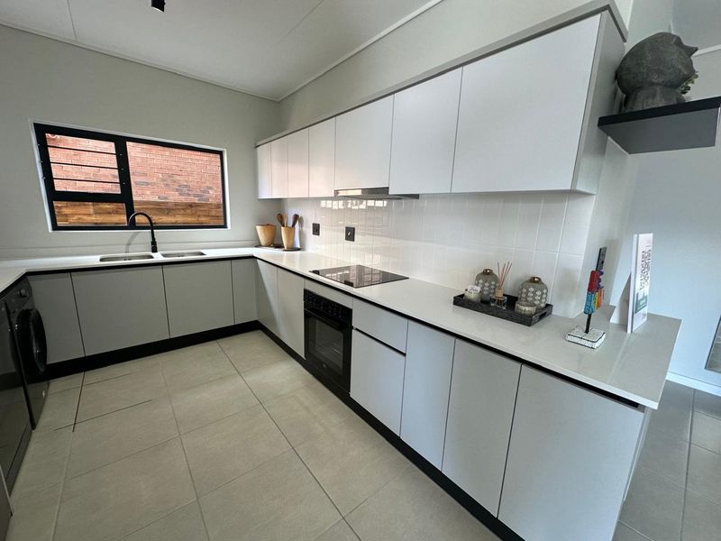 Modern kitchen featuring sleek white cabinetry, stone countertops, integrated appliances, a tiled backsplash, and a double sink with a contemporary black mixer tap.