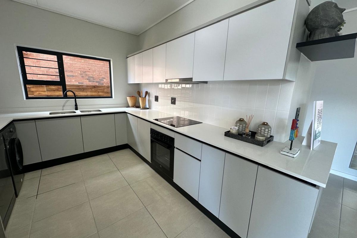 Modern kitchen featuring sleek white cabinetry, stone countertops, integrated appliances, a tiled backsplash, and a double sink with a contemporary black mixer tap.
