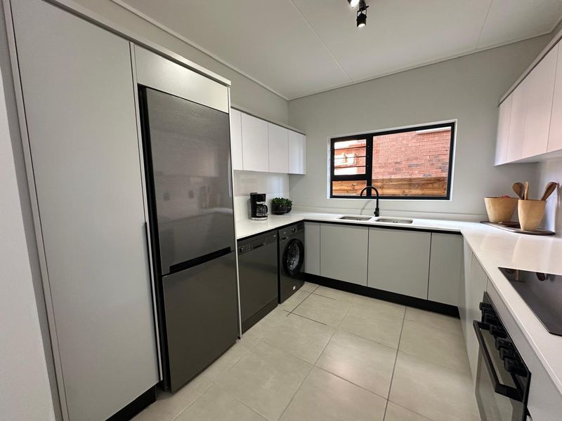 Modern kitchen featuring sleek cabinetry, stone countertops, integrated appliances, and a double sink with a contemporary black tap.