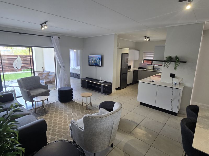Spacious open-plan living area featuring tiled floors, a modern kitchen with island, and seamless flow to an outdoor patio through large sliding glass doors.