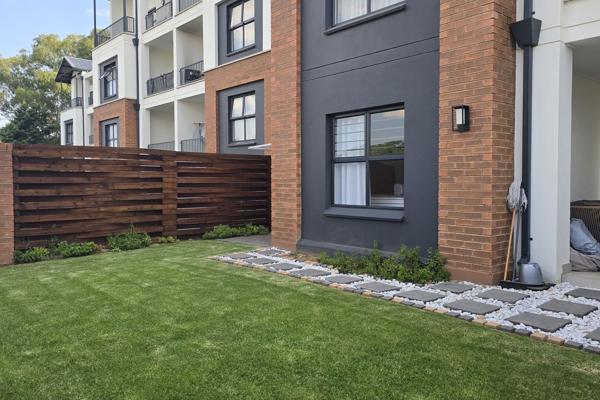 A well-maintained rear garden area featuring a manicured lawn, brick and timber privacy fencing, and a neat paved walkway with decorative stone borders.