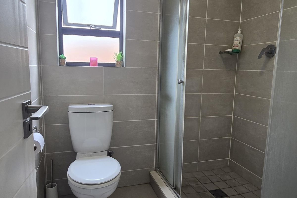 A compact bathroom featuring floor-to-ceiling neutral tiling, a glass-enclosed shower, and a standard toilet.