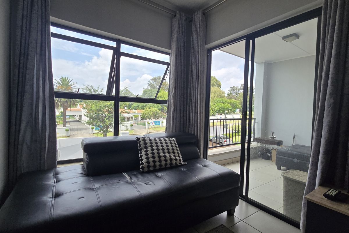 A living area featuring large windows and a sliding glass door that opens onto a private balcony with outdoor views.