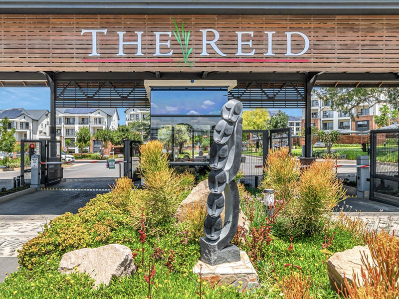 The secure entrance gate and guardhouse of The Reid residential estate, featuring modern signage and well-maintained landscaping.
