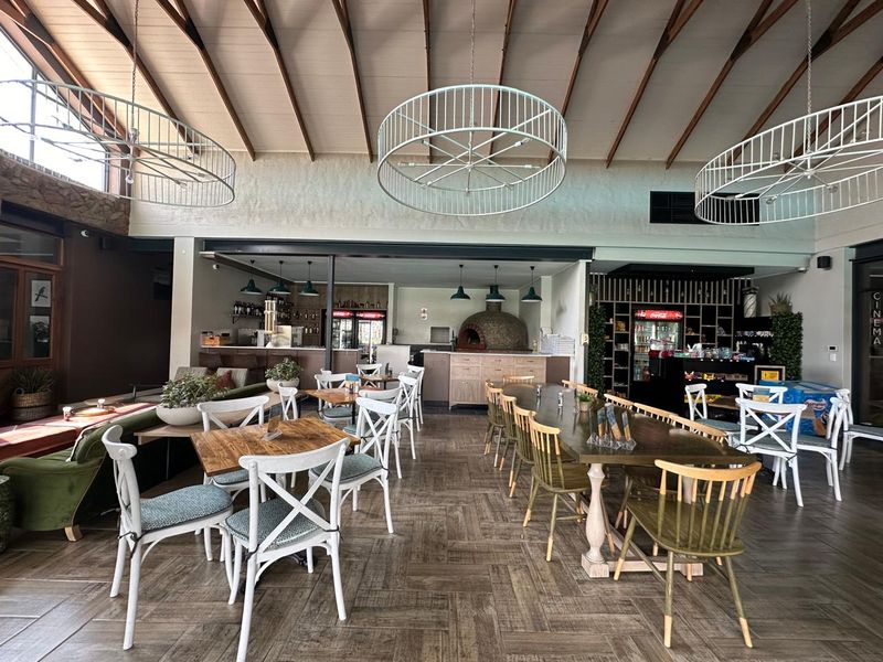 Spacious open-plan dining and bar area featuring high exposed beam ceilings, wood-look tile flooring, and a built-in pizza oven.