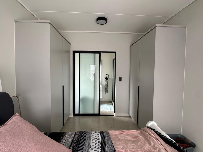 A modern bedroom featuring floor-to-ceiling built-in cupboards and a sleek sliding glass door leading to an en-suite bathroom.