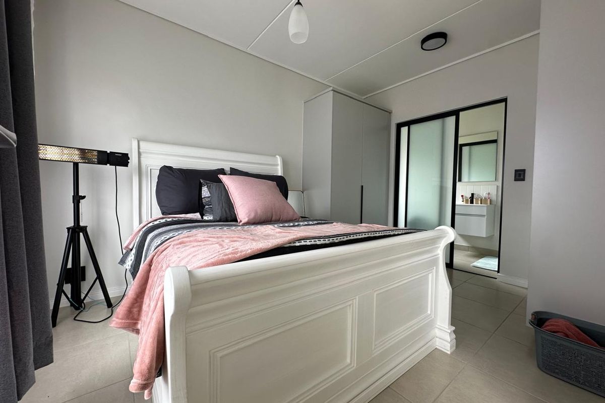 A well-maintained bedroom featuring tiled flooring, built-in wardrobe storage, and an en-suite bathroom accessible through a modern sliding door.