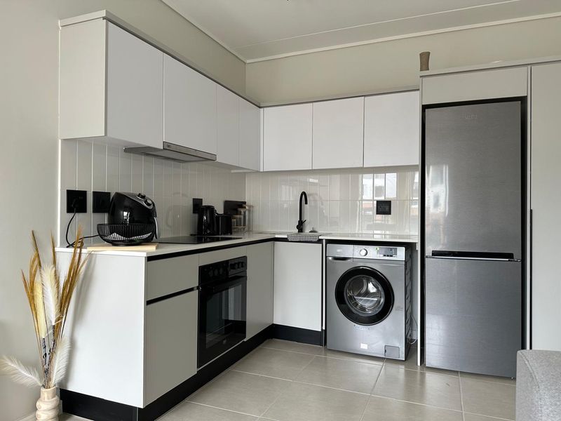 Modern compact kitchen featuring white cabinetry, subway tile backsplash, integrated oven, electric hob, and space for a washing machine and fridge.