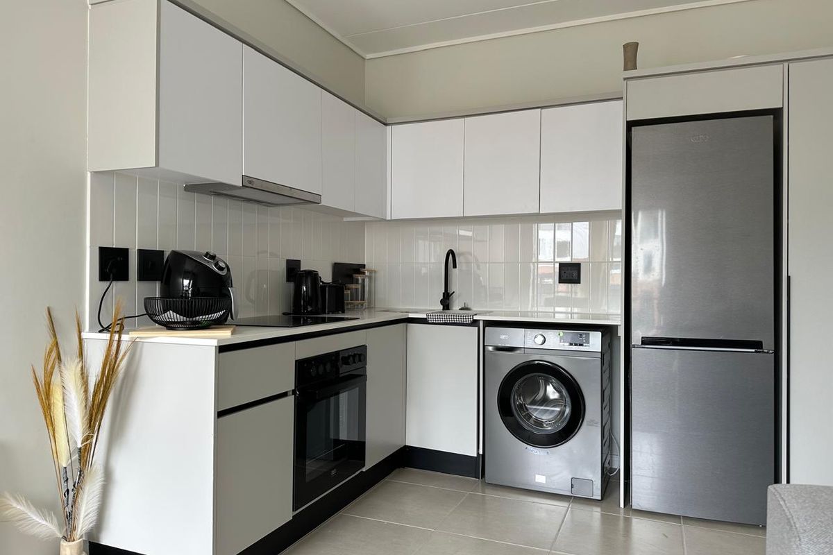 Modern compact kitchen featuring white cabinetry, subway tile backsplash, integrated oven, electric hob, and space for a washing machine and fridge.