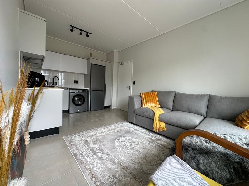 Modern open-plan living area featuring a compact kitchen with built-in cabinetry, tiled flooring, and contemporary track lighting.