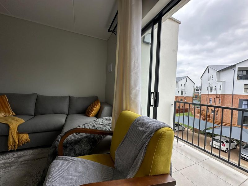 A living room featuring a sliding glass door that opens onto a tiled balcony with a metal balustrade overlooking the complex.