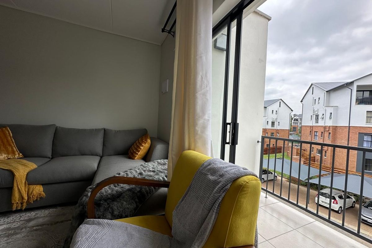 A living room featuring a sliding glass door that opens onto a tiled balcony with a metal balustrade overlooking the complex.