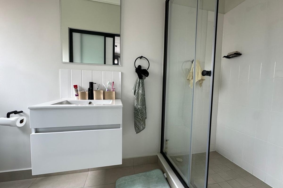 Modern bathroom featuring a wall-mounted vanity with integrated basin, a glass-enclosed shower with tiled walls, and neutral floor tiling.
