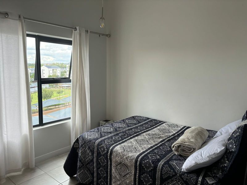 A bright bedroom featuring tiled flooring and a large window with views, providing a clean and functional living space.