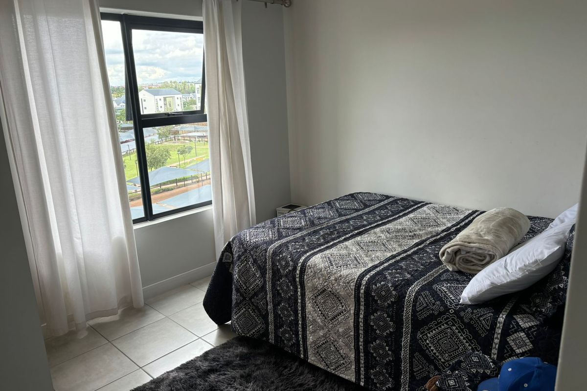 A well-lit bedroom featuring tiled flooring and a large window with views of the surrounding area.