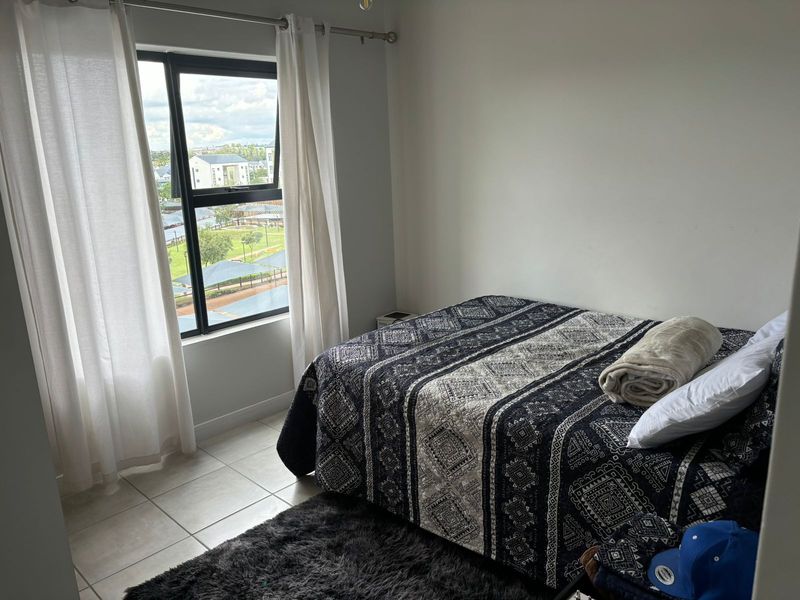 A well-lit bedroom featuring tiled flooring and a large window with views of the surrounding area.