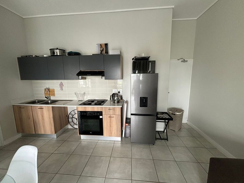 A functional kitchen featuring modern two-tone cabinetry, a built-in oven and hob, tiled backsplash, and neutral floor tiles.