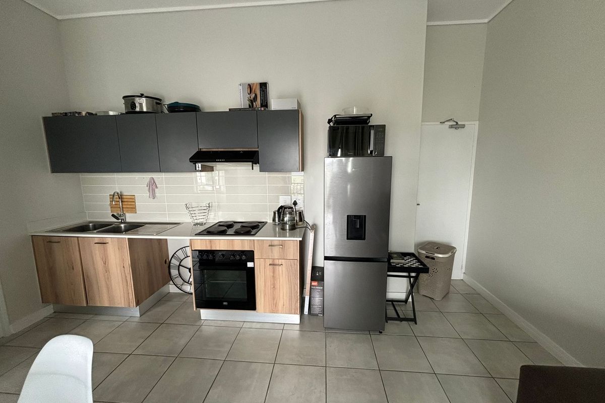 A functional kitchen featuring modern two-tone cabinetry, a built-in oven and hob, tiled backsplash, and neutral floor tiles.