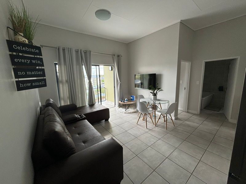 Open-plan living and dining area featuring neutral tiled flooring, high ceilings, and direct access to a private balcony through sliding glass doors.