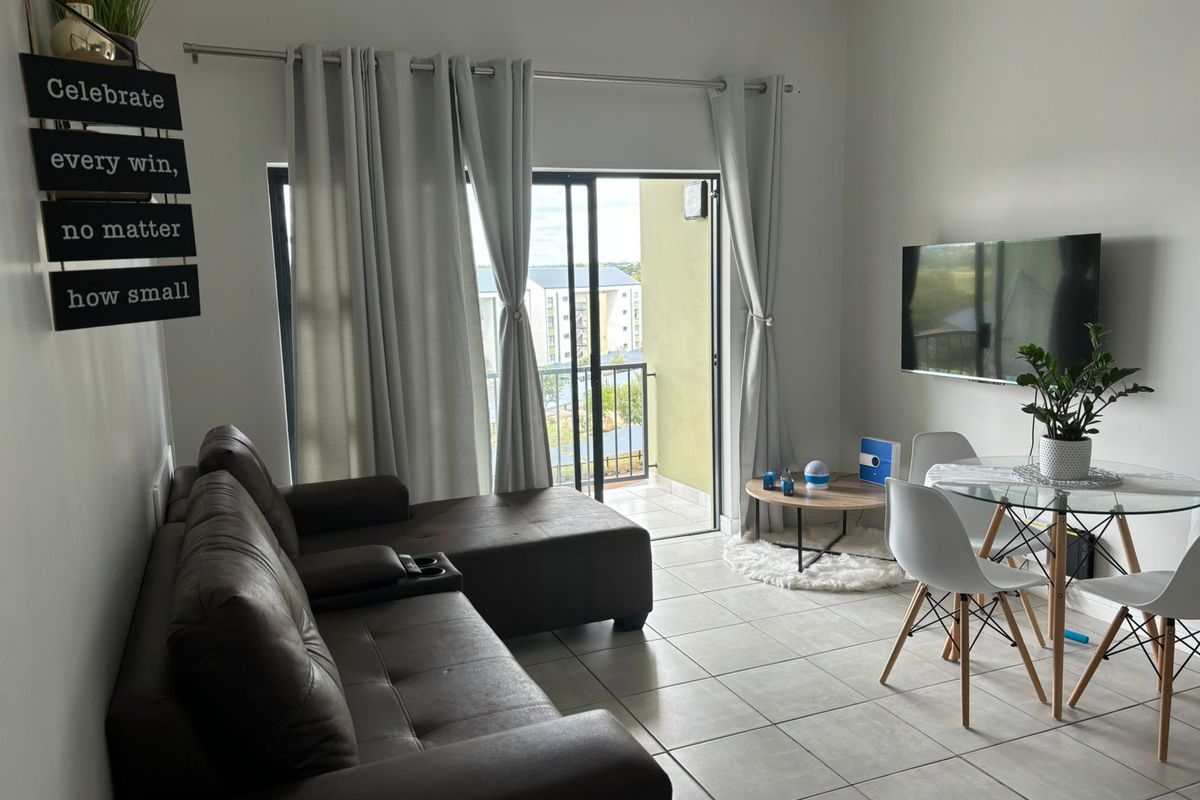 An open-plan living and dining area featuring tiled flooring, neutral walls, and a sliding glass door providing access to a private balcony.
