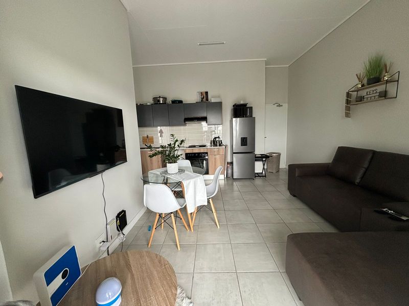 Open-plan living area featuring a modern kitchen with built-in cabinetry, tiled flooring, and a functional layout connecting the kitchen and lounge space.