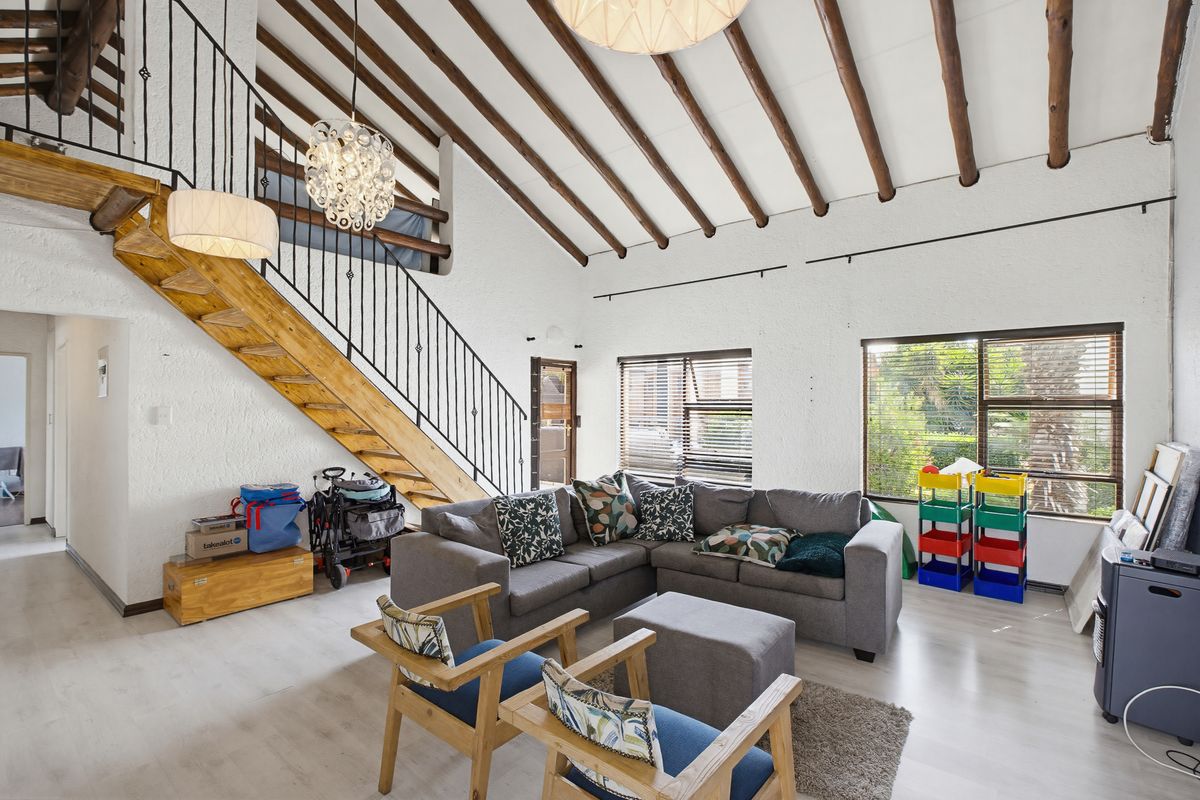 Spacious living room featuring high vaulted ceilings with exposed timber beams, a timber staircase with wrought iron railing, and large windows with venetian blinds.