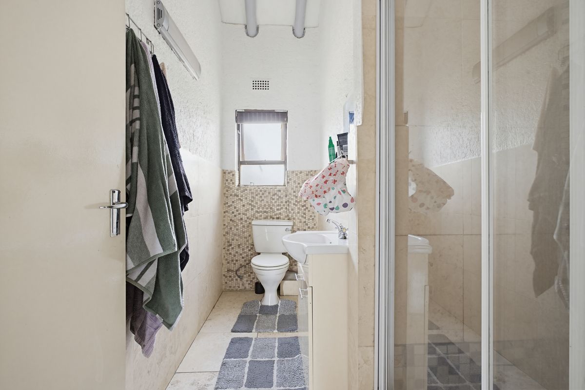 A functional bathroom featuring a pedestal basin, toilet, and a glass-enclosed shower with neutral wall and floor tiling.