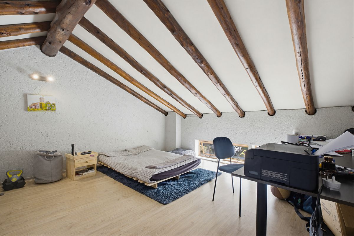 Attic-style bedroom featuring exposed timber ceiling beams, textured walls, and laminate flooring with a low-level window providing natural light.