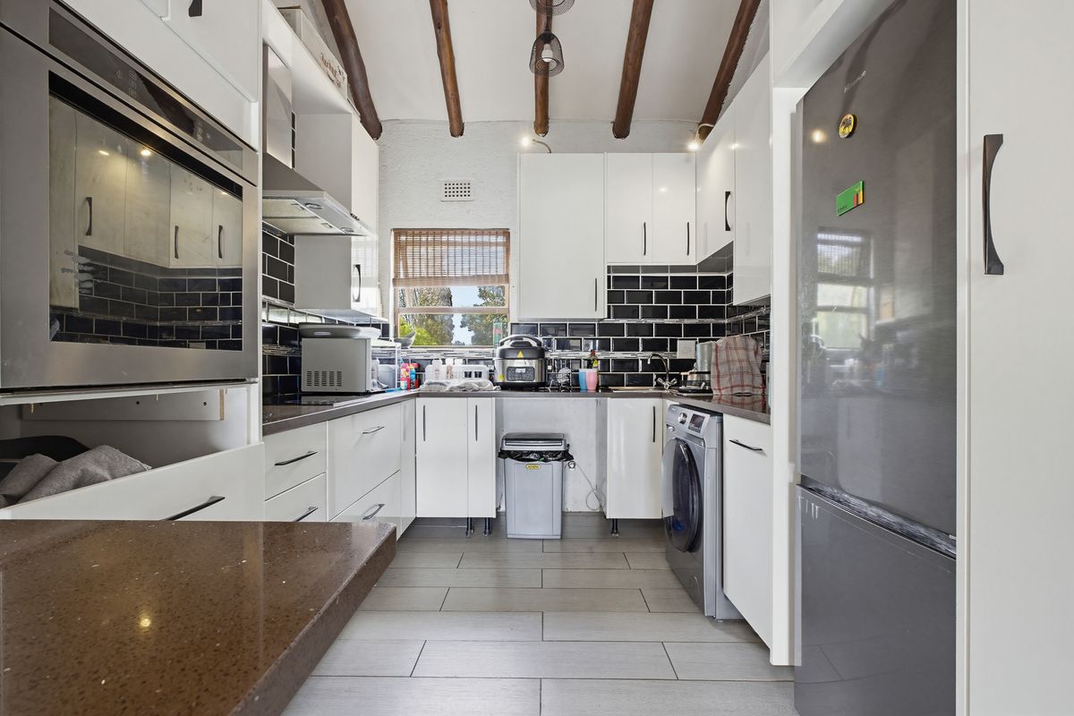 A functional kitchen featuring white cabinetry, dark subway tile backsplash, stone countertops, and exposed timber ceiling beams, providing a modern yet rustic aesthetic.