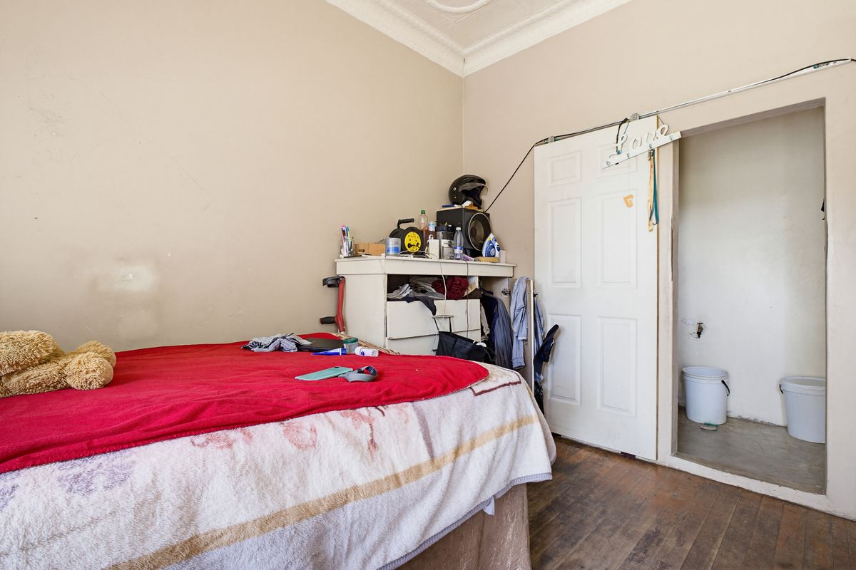 A bedroom featuring original timber flooring, decorative ceiling cornice, and an adjoining small utility space or en-suite area.