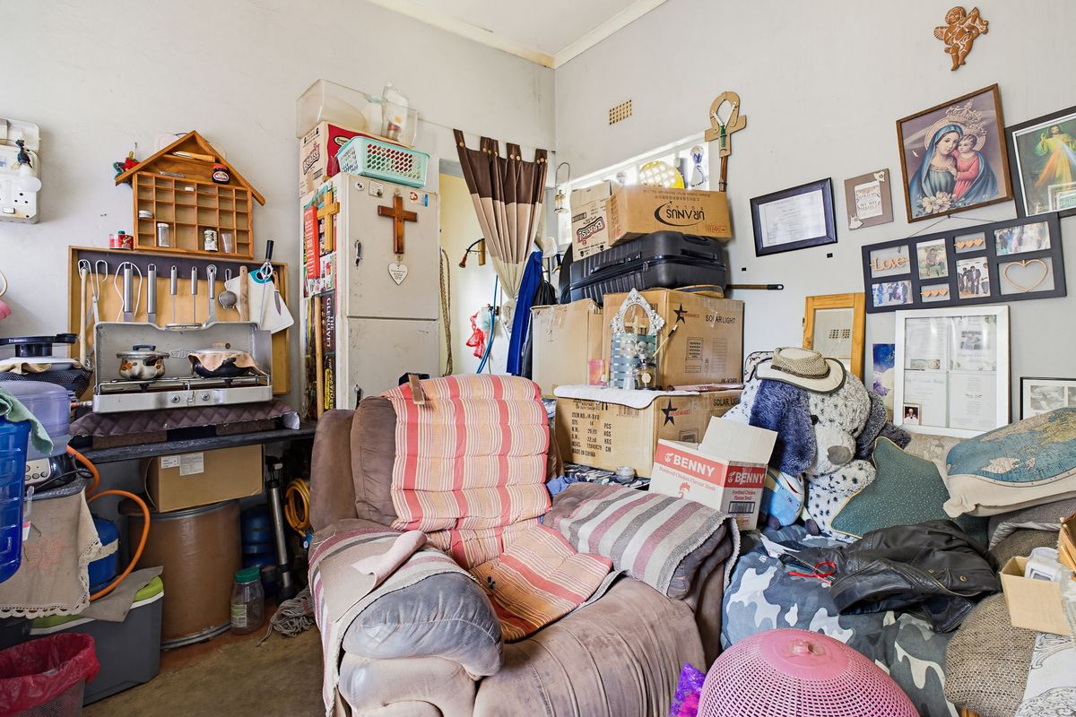 A cluttered utility or living space featuring basic wall finishes and fixed structural elements, currently used for storage and daily living.