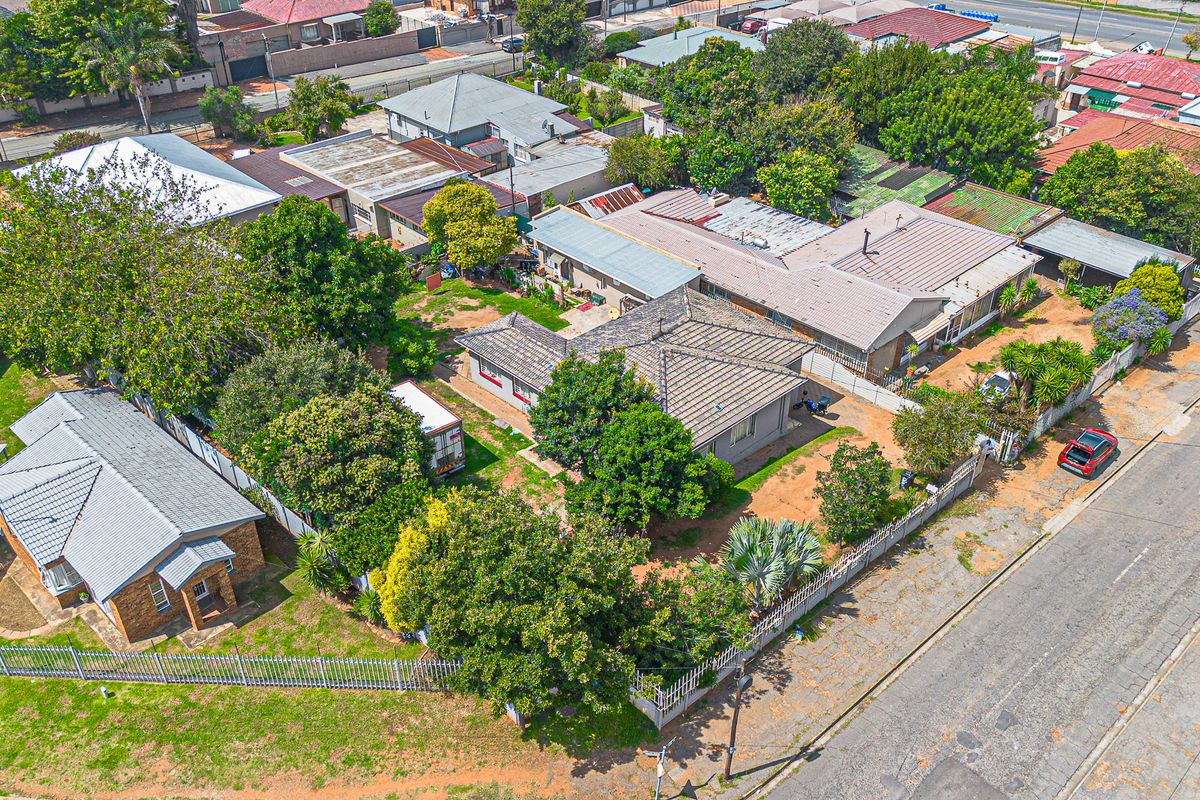 Aerial view of a residential property featuring a tiled roof house, established garden, and perimeter fencing in a suburban neighborhood setting.