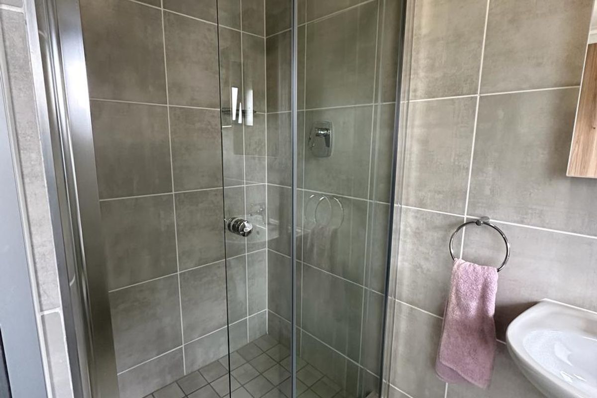 Modern bathroom featuring a glass-enclosed walk-in shower with neutral wall tiles and a pedestal basin.