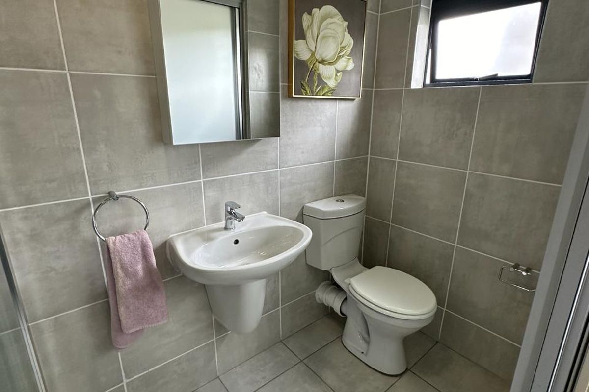 A modern guest bathroom featuring neutral floor-to-ceiling wall tiles, a pedestal basin, a wall-mounted mirror, and a standard toilet.